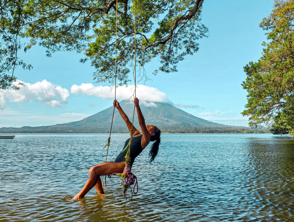 me sitting at a swing on a bright blue sunny day at a freshwater lake in Ometepe, Nicaragua, Central America and at the background is Volcano Mount Conception
